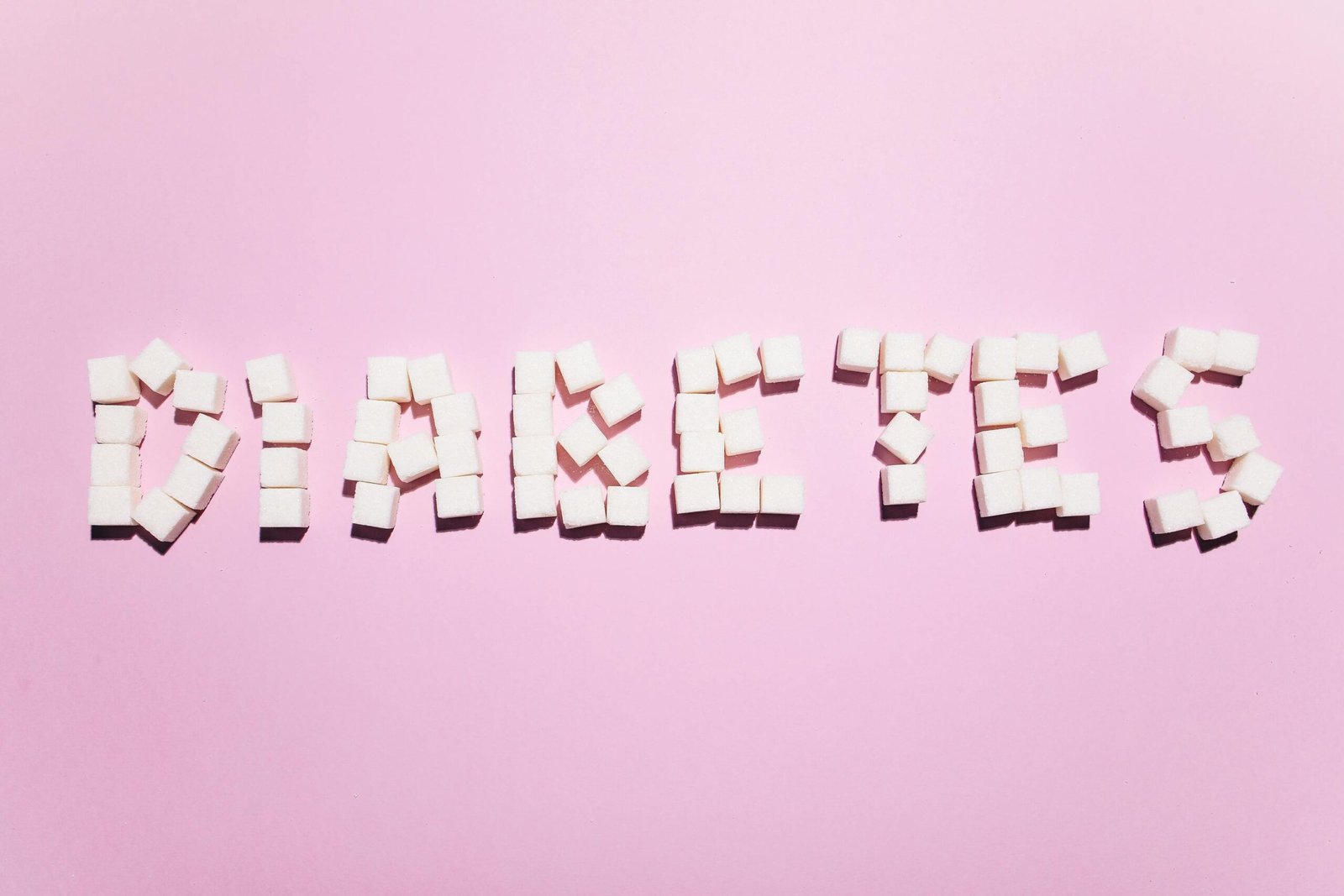 Sugar cubes form the word 'Diabetes' on a pink surface, highlighting health concern.